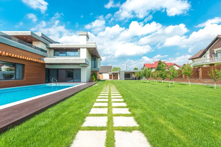 A long rectangular swimming pool alongside a dark wooden deck, with a broad green lawn and a stepping-stone path beside it.